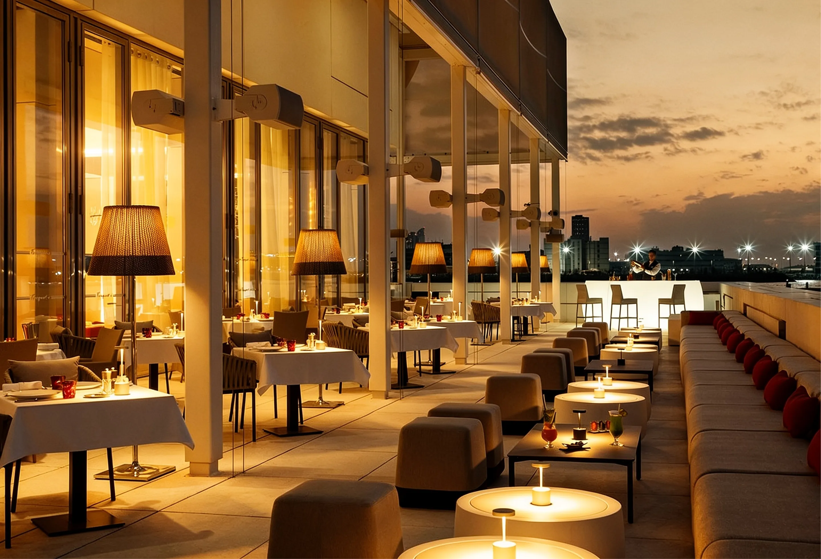 A terrace at the Louvre Abu Dhabi at dusk: tables set, lamps lit, and the city's lights across the water